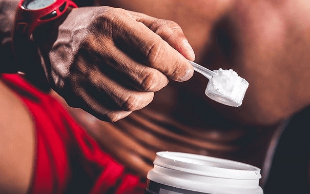 Hombre en ropa deportiva con un scoop de creatina en la mano.